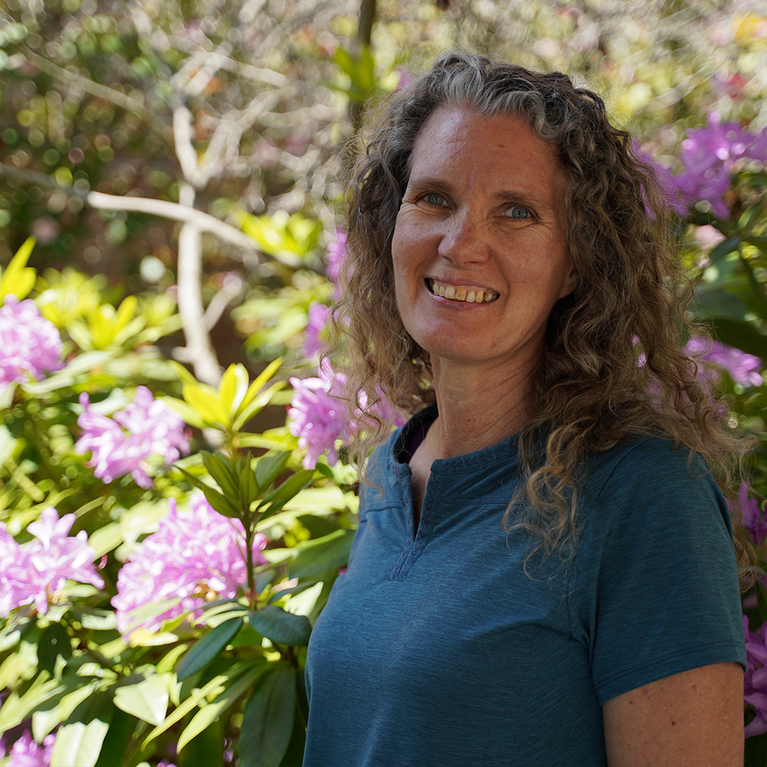 Women smiling in front of bushes with pink flowers.